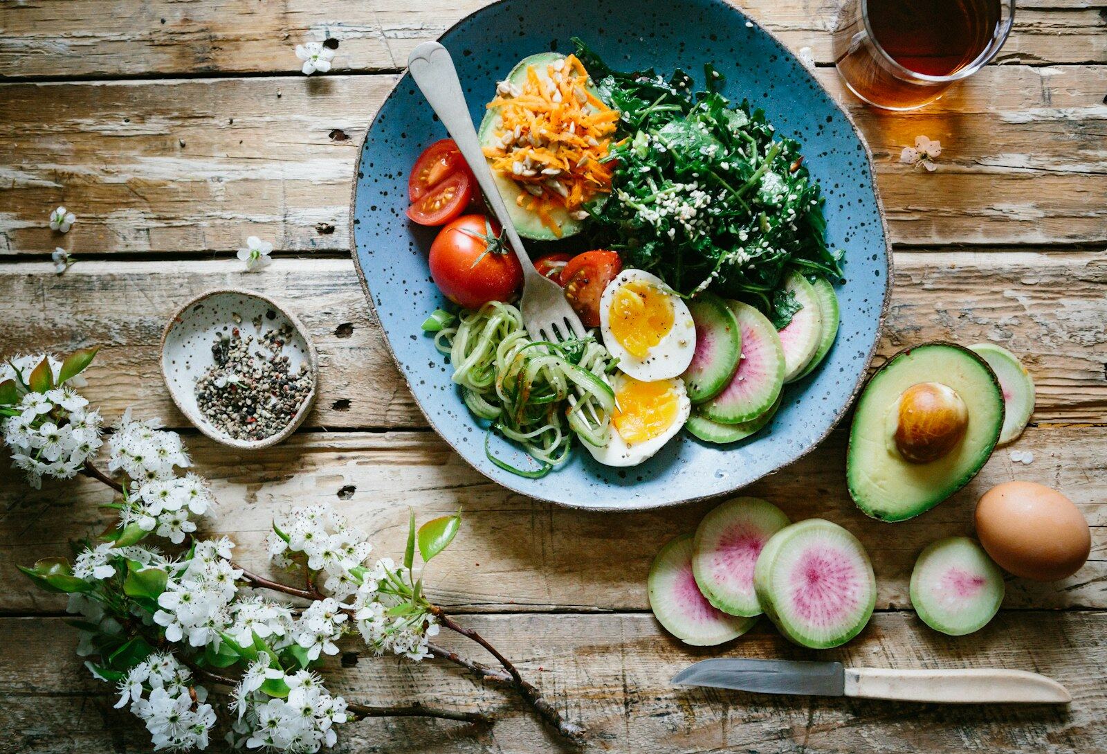 A bowl of vegetables, eggs and avocado on a wooden table