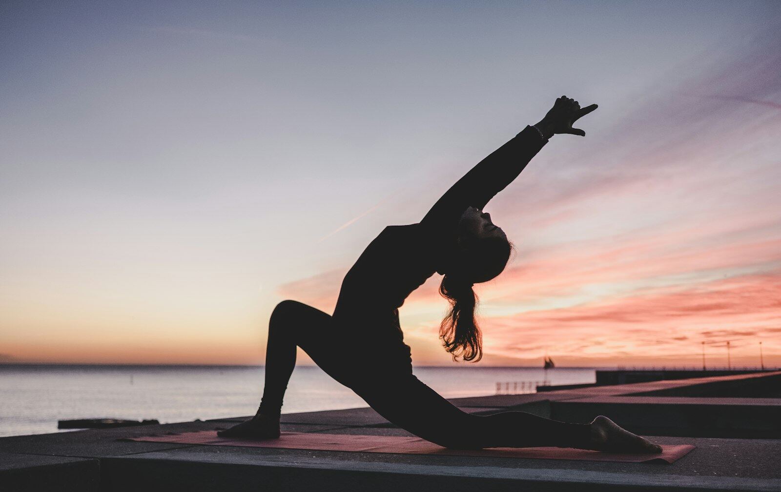 A person stretching on a yoga mat at sunset